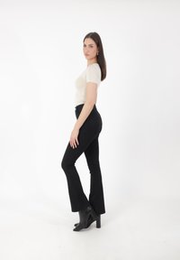 T-shirt beige ajusté, jeans évasés noirs et bottines à talons noirs. La tenue est minimaliste avec une texture lisse et une coupe ajustée.