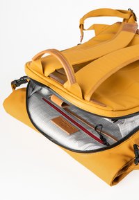 Zaino giallo con spallacci imbottiti, maniglia superiore, scomparto principale con zip e interno grigio che presenta una tasca con zip rossa e una patch con logo.