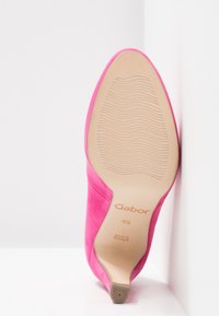 Chaussure à talon haut en daim rose, à bout pointu. Dispose d'une semelle lisse marron clair avec une texture antidérapante et un logo sur la semelle intérieure.