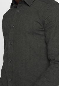 Ciemnoszara koszula w jodełkę z kołnierzykiem zapinanym na guziki; wyposażona w plastikowe guziki i teksturowane wykończenie tkaniny.