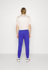 Mönstrad kortärmad skjorta i vitt med orange geometrisk design, kombinerad med blå sweatpants med en bakficka och ribbade mudd.