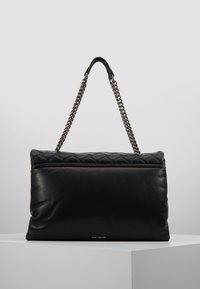 Czarna skórzana torebka z pikowanym górnym odcinkiem, srebrnym łańcuszkiem na ramie, miękką teksturą i detalem logo na dolnej przedniej części.