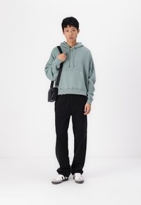 Grøn hættetrøje med kengurutaske, sorte loose-fit jeans og hvide sneakers med grå detaljer. Tilbehør: lille sort skuldertaske.
