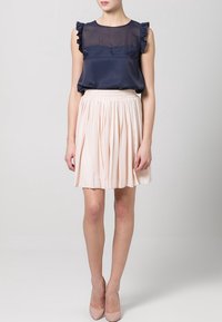 Navy satin top with ruffled sleeves, paired with a light pink pleated skirt. Smooth texture and an elastic waistband, completed with beige heels.