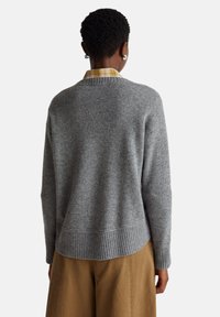 Šedý vlněný svetr s žebrovaným lemem a manžetami, kulatým výstřihem, nošený přes žlutou kostkovanou košili, vykazující uvolněný střih.