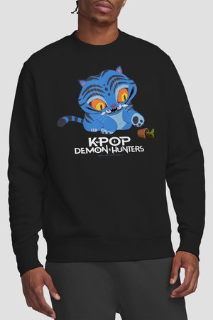 Man wearing black sweatshirt with a blue cartoon tiger playing with a tipped plant and text "KPOP DEMON HUNTERS" on front.