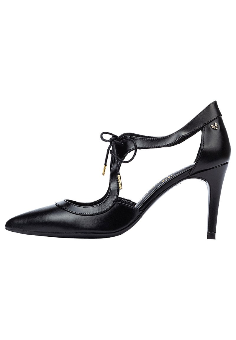 Zapato de tacón alto de cuero negro con punta afilada, lados recortados y detalle de lazo. Presenta acentos dorados y un tacón delgado.