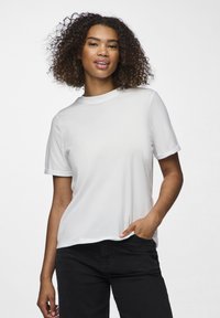 Weißes Baumwoll-T-Shirt mit kurzen Ärmeln, geripptem Ausschnitt und lässiger Passform; getragen mit schwarzen Jeans, was die Schlichtheit und Vielseitigkeit betont.
