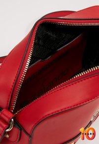 Borsa a tracolla in pelle rossa con chiusura a zip, fodera nera con stampa del logo e dettagli della zip in tono oro. L'interno mostra l'etichetta del marchio.