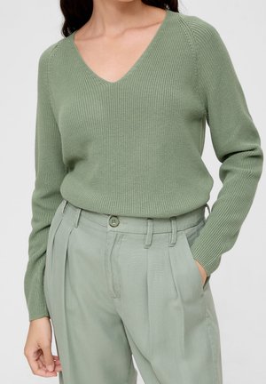 Pull vert en V avec une texture côtelée, associé à un pantalon plissé vert clair. Le pull a des manches longues et une taille cintrée.