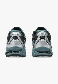 Scarpe da corsa nere e verde turchese con accenti argentati, dotate di una tomaia in rete, suola imbottita e un design posteriore distintivo con dettagli riflettenti.