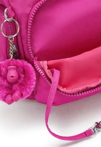 Pink fabric bag with a furry pink keychain and a zippered compartment. Features a smooth texture and contrasting inner lining.
