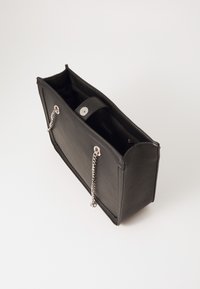 Geantă de piele neagră cu o formă structurată, accente din lanț argintiu și închidere tip clapetă, având o textură netedă și un interior deschis.