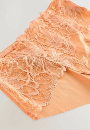 Perzikkleurige lingerie met ingewikkelde kantdetails en gegolfde randen, met een gladde binnenstof en subtiele gouden accenten.