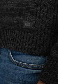 Donkergrijs gebreid sweater met een ribgebreide onderrand, label met de tekst "Patrol Industries," gecombineerd met blauwe spijkerbroeken.
