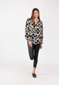 Blusa a maniche lunghe con motivo floreale in nero e beige, dotata di colletto e vestibilità morbida, abbinata a leggings neri aderenti e ballerine.