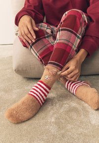 Karvased pruunid sokid punaste ja valgete triibuliste kantidega, millel on komme kujutavad mustrid. Kandatud ruudulise öösärgi alumise osaga, tekstuurse vaiba peal.