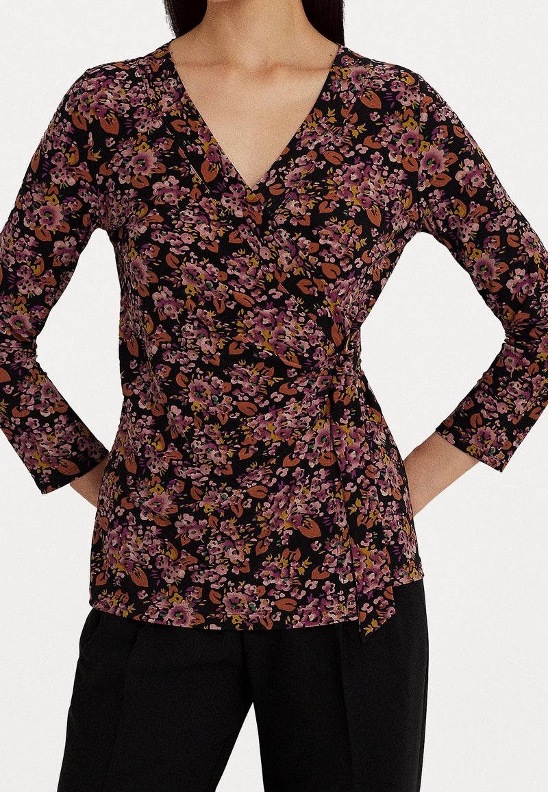 Svart blommig omslagstopp med trekvartsärmar, prydd med rosa och orange blommor och blad, mjuk textur och en sida med knytning.