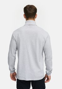 Camisa gris de manga larga con cuello alto, con una tela texturada y sutiles ribetes, mostrada desde atrás con pantalones oscuros.