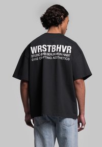 Black oversized t-shirt made of cotton. Features white text on the back: "WRSTBHVR," "STUDIO (030) BERLIN MON HABIT," and "0102 CRAFTING AESTHETICS."
