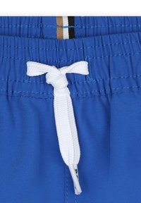 Costumi da bagno blu realizzati in un tessuto testurizzato, con un laccio bianco, una vita elastica e sottili accenti a strisce sopra la vita.