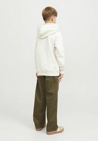 Sudadera crema con una gran capucha, combinada con pantalones de pierna ancha en color verde oliva. Texturas ligeras y tonos neutros dominan el conjunto.