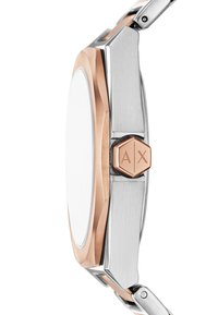 Srebrny i różowozłoty metalowy zegarek z ośmiokątną kopertą, polerowaną białą tarczą oraz sześciokątną różowozłotą koronką. Posiada bransoletę z metalowych ogniw.