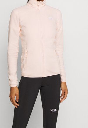 Veste en polaire rose clair avec un col haut, une fermeture éclair à l'avant et deux poches latérales ; présente le logo North Face sur la poitrine.