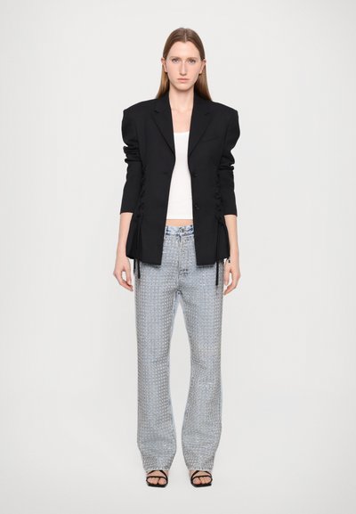 Black tailored blazer with padded shoulders, button closure, and ruched detailing. Light blue patterned straight-leg trousers with side zippers.