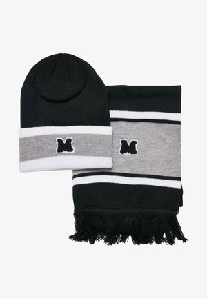 Melnā cepure un saskaņota šalles komplekts ar pelēkām svītrām un baltām akcentiem. Abiem izstrādājumiem ir mazs melns logo uzlīme. Šallei ir frizētas malas.