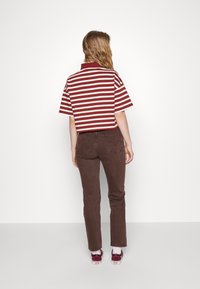 Randig röd och vit kortärmad polo skjorta, kombinerad med bruna jeans, bärs med bordeauxfärgade sneakers med vita sulor.