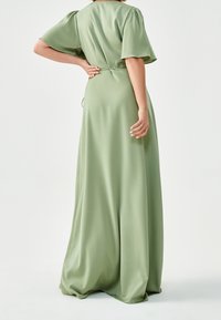 Lång, flödande klänning i ljusgrön tyg med korta puffärmar och en midja med knytning, med en slät, sidentystliknande textur.