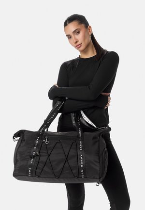 Tumehalli naine musta pikkade varrukatega ülaosaga hoiab käes suurt musta spordikotti, millel on valged "Cardio Bunny" kaubamärgiga rihmad.