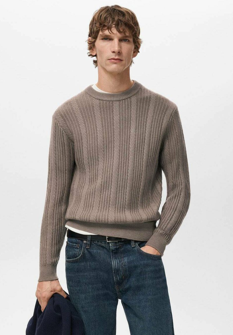 Grijs geribd trui met een ronde hals, gecombineerd met donkere spijkerbroek. Opvallende textuur en nauwsluitend ontwerp zijn duidelijk zichtbaar.