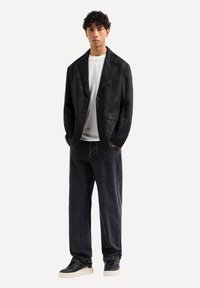 Blazer nero strutturato con doppi bottoni, abbinato a una t-shirt bianca e jeans neri larghi. Sneaker nere con suola crema completano l'outfit.