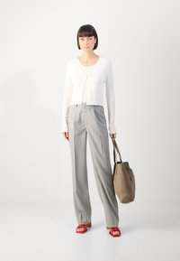 White cropped cardigan, gray pinstriped trousers, red strappy sandals, and a gray tote bag; smooth texture and relaxed fit.