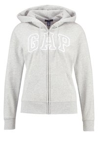 Sudadera con cremallera en color gris, hecha de un tejido suave y texturizado. Presenta un bolsillo frontal, capucha con cordón y el logo "GAP" en blanco en el pecho.