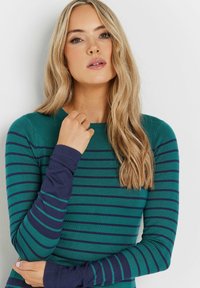 Tee mit langen Ärmeln in Türkis mit navyblauen horizontalen Streifen. Hat eine gerippte Textur und eine enganliegende Passform. Umgekrempelte Manschetten in navyblau.