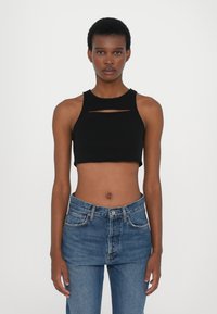 Top court noir sans manches avec un col rond, présentant un détail de découpe horizontal. Assorti à un jean en denim bleu taille haute.