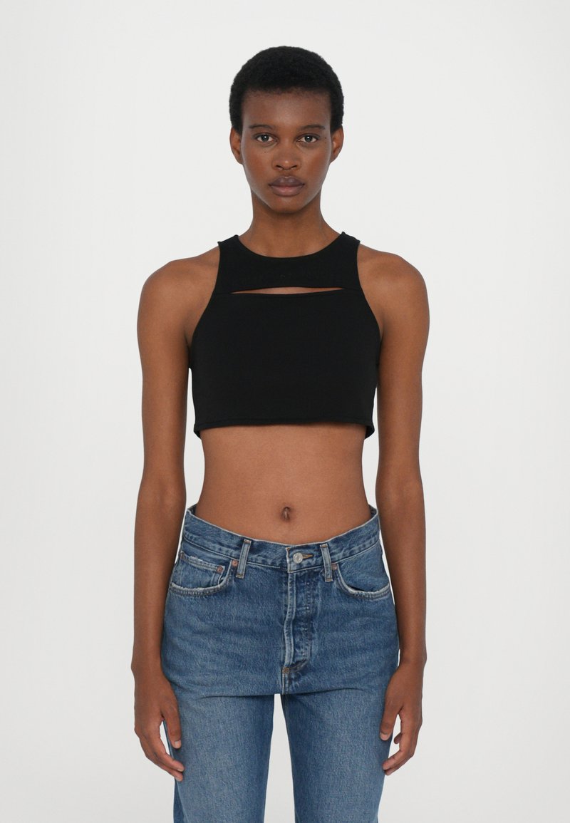 Top court noir sans manches avec un col rond, présentant un détail de découpe horizontal. Assorti à un jean en denim bleu taille haute.