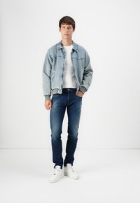 Valkoinen denim-takki, jossa on joustavat hihansuut, valkoinen pyöreä kauluspaita, tummansiniset slim-fit farkut ja valkoiset tennarit. Yksinkertainen muotoilu, rento istuvuus.