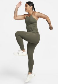 Top atletico verde oliva e leggings, materiale elasticizzato, design aderente, con tasca laterale sui leggings, abbinato a sneakers bianche.