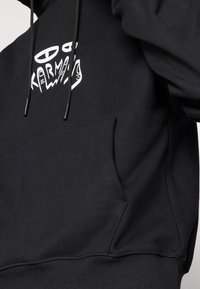 Black hoodie featuring a white graphic logo, adjustable drawstrings, and a kangaroo pocket, made from cotton blend fabric.