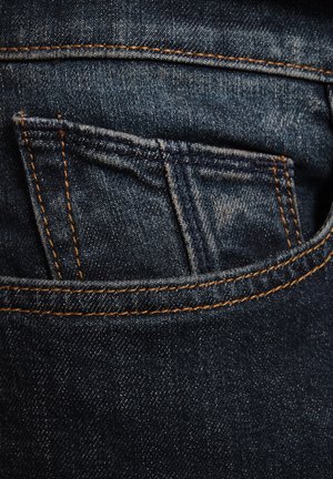 Mörkblå denimjeans har en bakficka med orange sömnad och en något slitagen yta, vilket visar på en praktisk design.