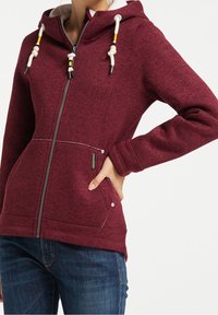 Bordowa bluza z zamkiem błyskawicznym o strukturze fleece, kontrastowe białe wykończenia, regulowany kaptur z kolorowymi sznurkami, oraz detale kieszeni bocznych.