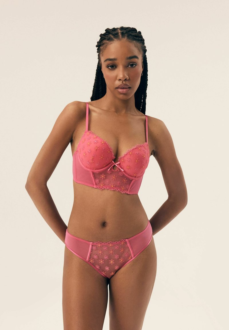 Różowy zestaw bielizny składający się z poduszki braletki z kwiatowym haftem oraz pasujących majtek bikini z prześwitującymi panelami i falbaniastymi krawędziami.