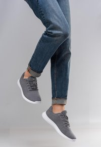 Baskets grises en tricot avec semelles blanches, dotées d'un système à lacets et d'un bout arrondi. Portées avec un jean en denim retroussé.