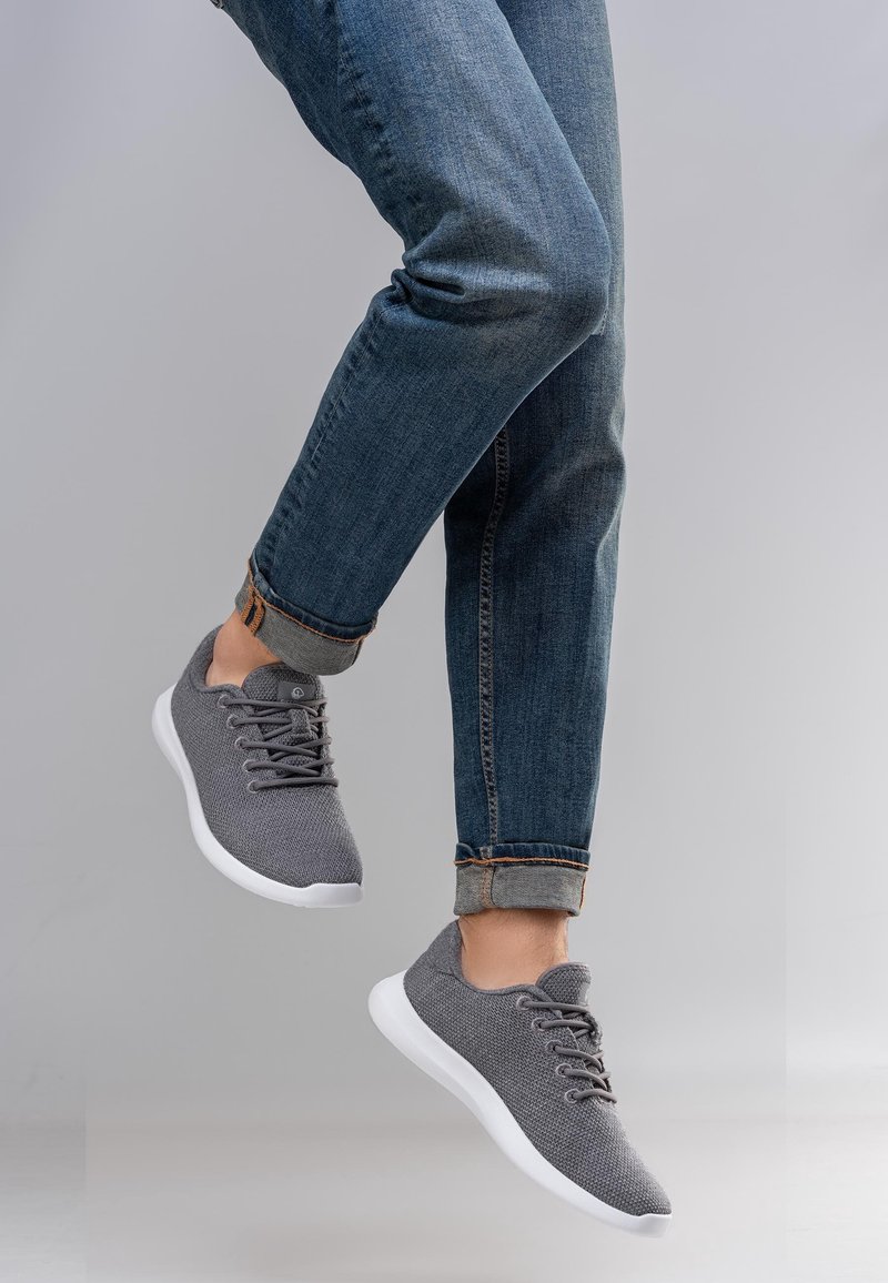 Baskets grises en tricot avec semelles blanches, dotées d'un système à lacets et d'un bout arrondi. Portées avec un jean en denim retroussé.