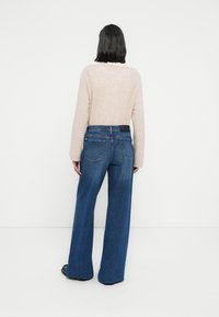 Ανοιχτό ροζ πουλόβερ με μακριά μανίκια σε συνδυασμό με ψηλόμεσα, φαρδιά σκούρα μπλε τζιν, που αναδεικνύουν ένα απαλό ύφασμα με διακριτική υφή.