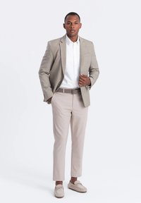 Blazer gris clair avec un col à revers, chemise blanche, pantalon beige et mocassins de couleur claire, présentant une coupe épurée et des détails minimalistes.